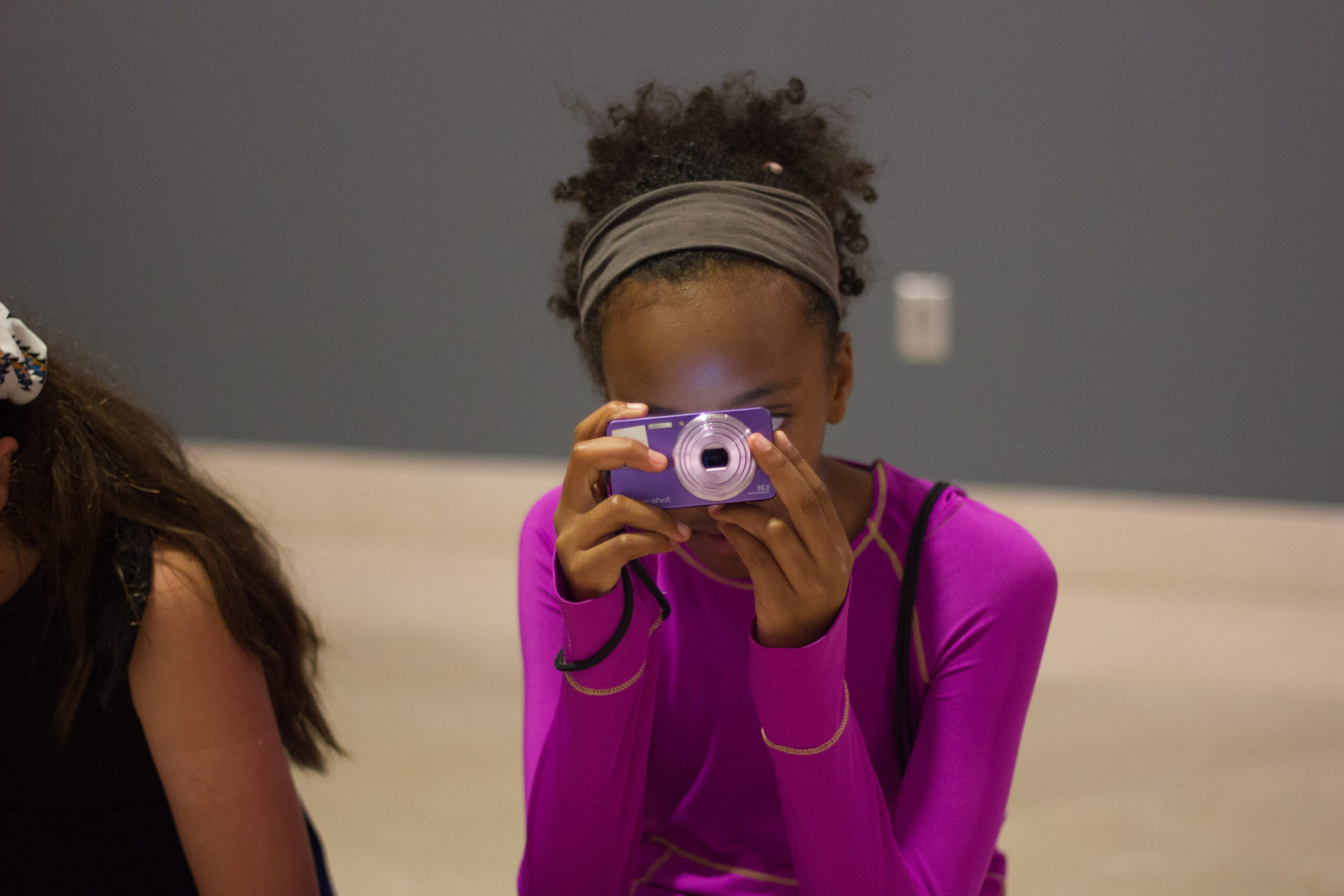 A child holding a purple camera up to her face while taking a photo.