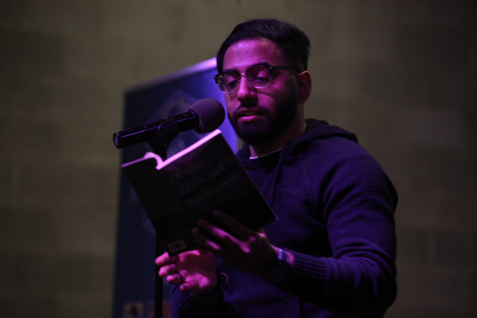 A person reading from a book and standing at a microphone.