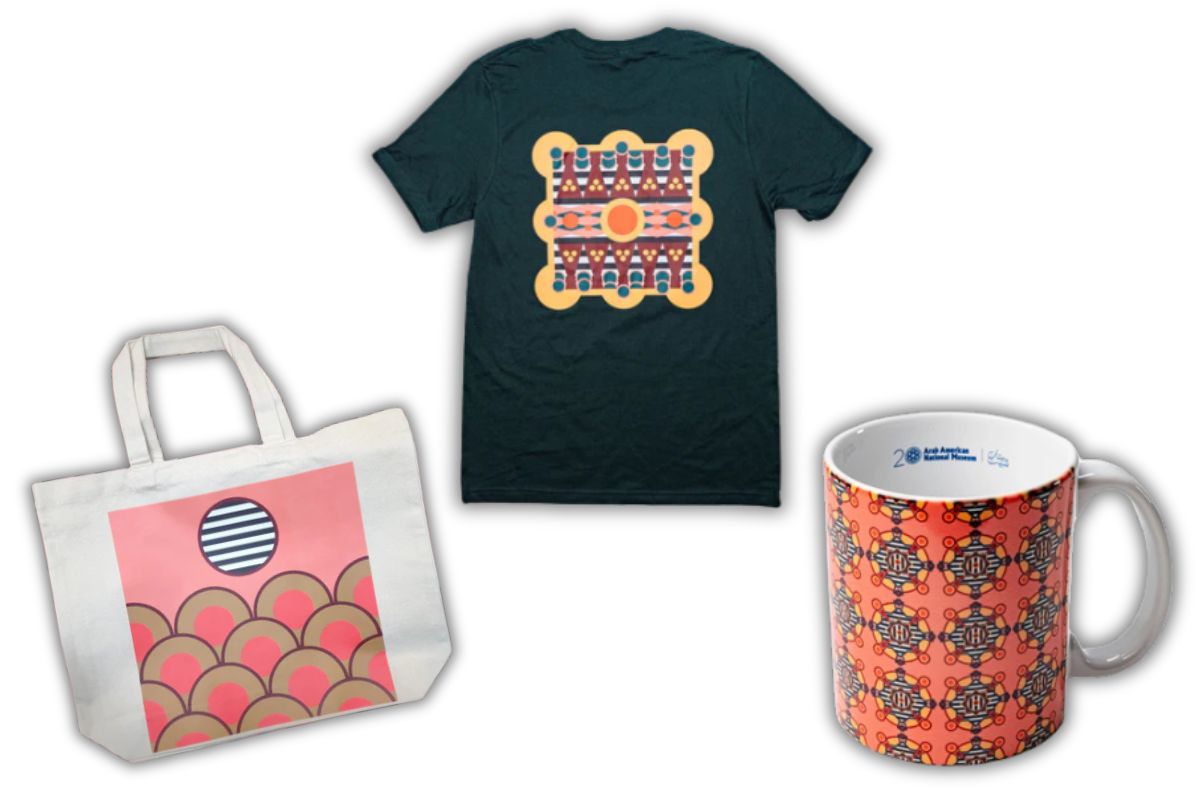 Image featuring three items from the AANM x Dahlia Elsayed 20th Anniversary Collection: a cream canvas tote bag with a pink and gold geometric design, a forest green t-shirt with a symmetrical abstract pattern on the back, and a ceramic mug with repeating orange and black artwork.