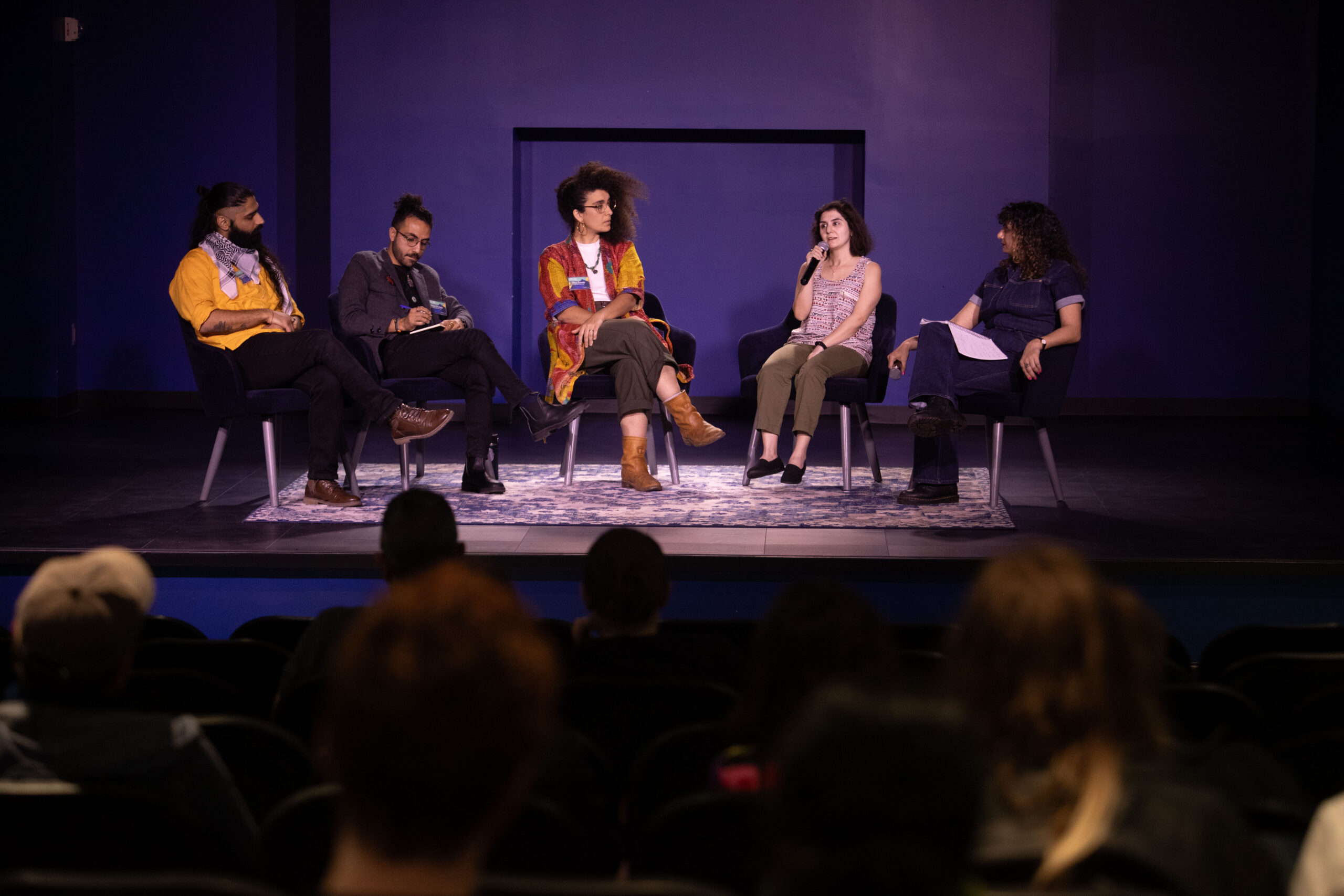 Panelists share insights during a featured conversation at the 2025 Arab American National Museum Film Festival. Five panelists speak on stage at the 2025 Arab American Film Festival, seated in a semicircle facing an audience.